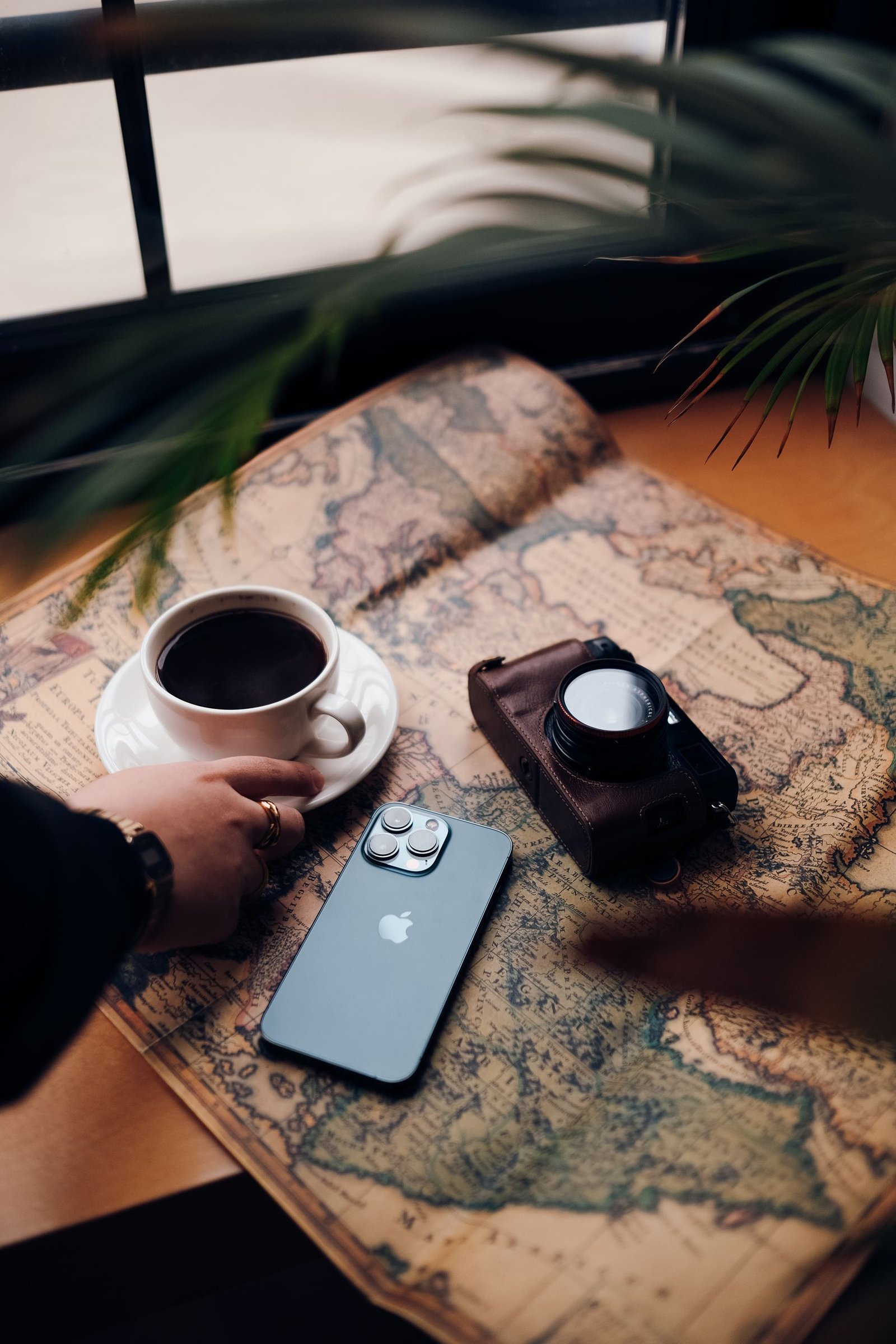 A cozy travel scene featuring a coffee cup, smartphone, and vintage camera on an old map.