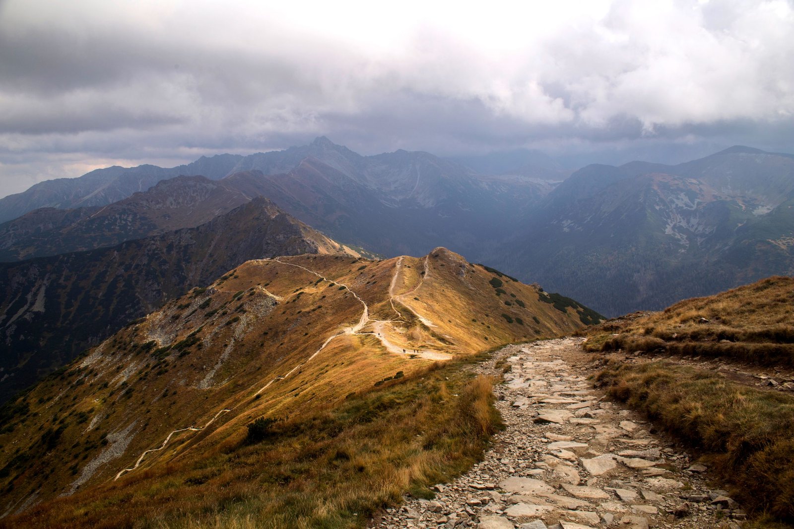 A rocky mountain pathway under a dramatic cloudy sky offering a serene and adventurous scene.