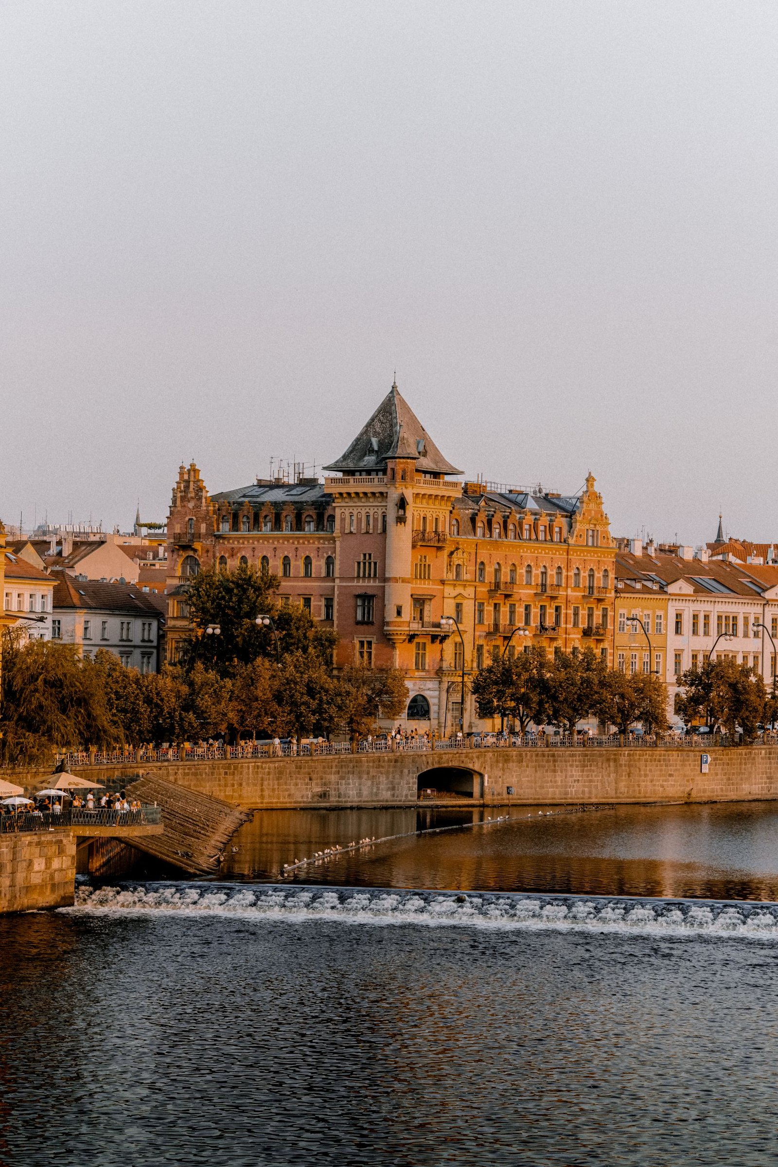 Scenic view of a historic European building by a tranquil river at sunset.