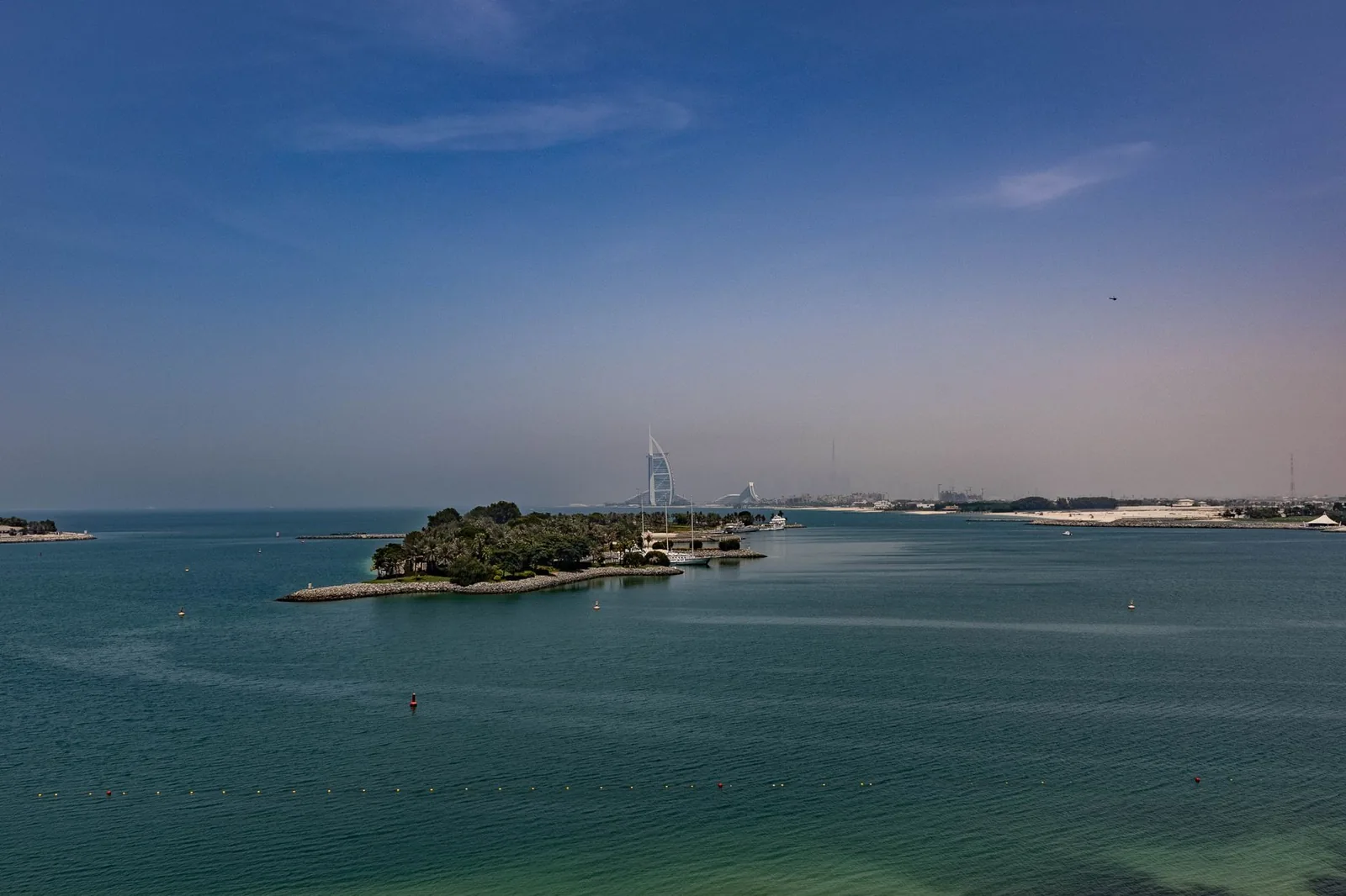 Aerial view of Dubai's coastline with Burj Al Arab in the distance under a clear blue sky.