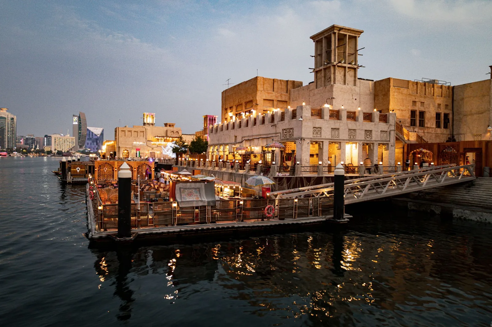 Charming view of Dubai Creek's waterfront with illuminated buildings and a bustling restaurant scene.