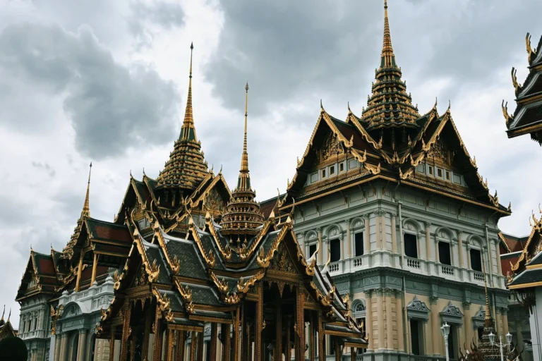 A beautiful view of the ornate rooftops of the Grand Palace in Bangkok, Thailand, under a cloudy sky.