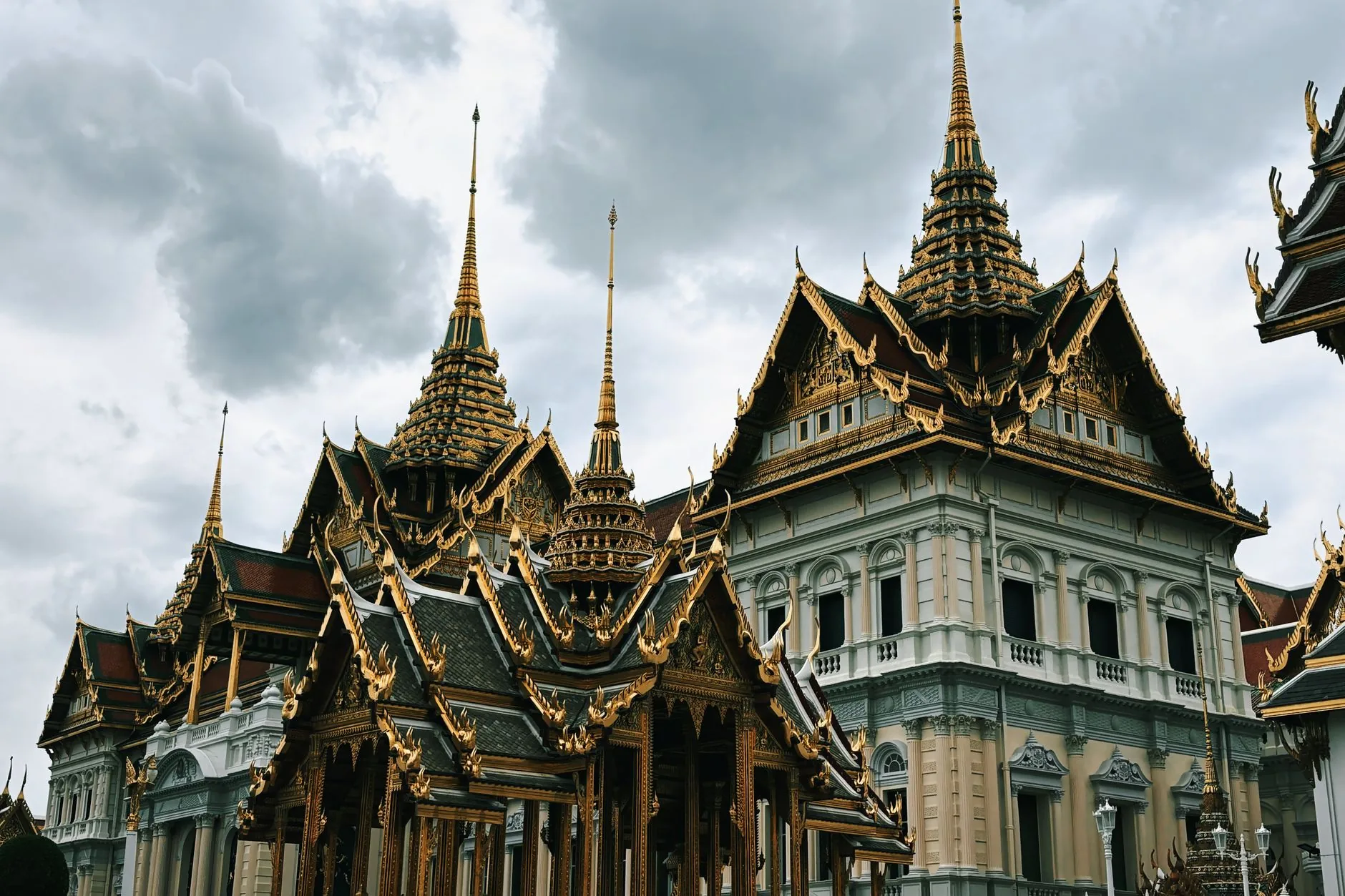 A beautiful view of the ornate rooftops of the Grand Palace in Bangkok, Thailand, under a cloudy sky.