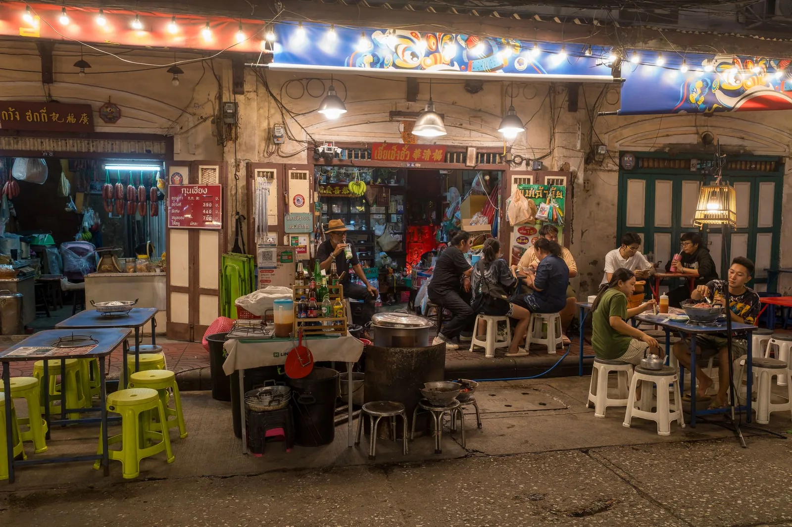 Nighttime street food scene in Bangkok with people dining outdoors under warm lights.