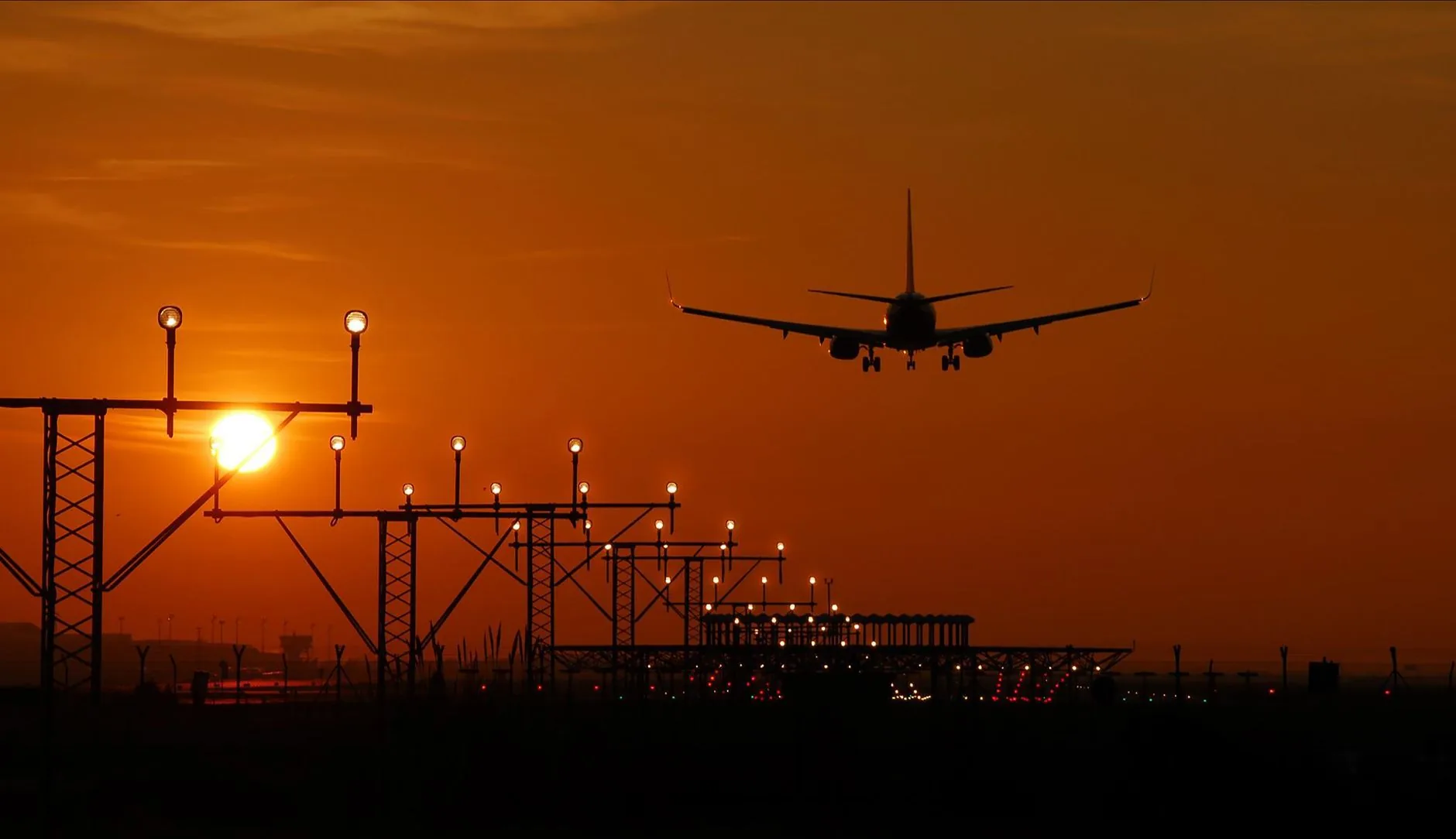 Silhouette of an airplane landing during sunset at Barcelona airport, with a vibrant orange sky.