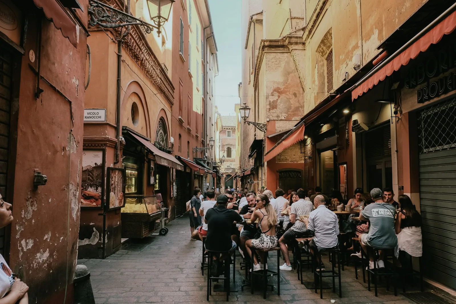 People dining together on a lively street in Bologna, Italy, surrounded by historic architecture.