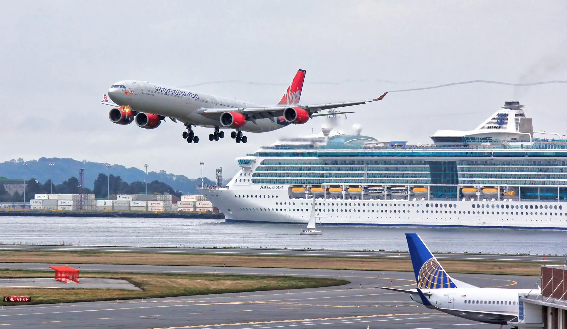 A thrilling view of an airplane landing with a cruise ship passing by in Boston Harbor.