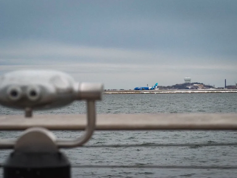 View of an airplane at Boston Harbor with distant industrial landscape and winter settings.
