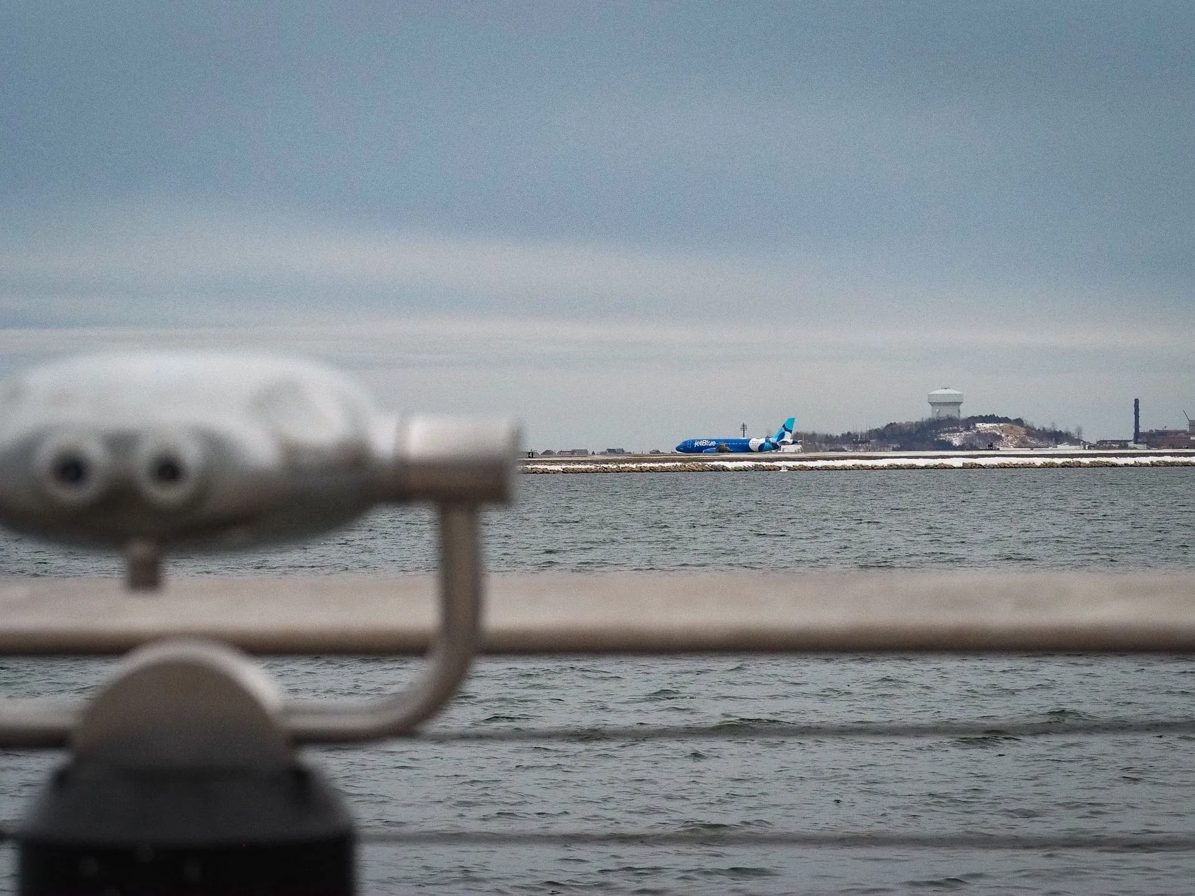 View of an airplane at Boston Harbor with distant industrial landscape and winter settings.