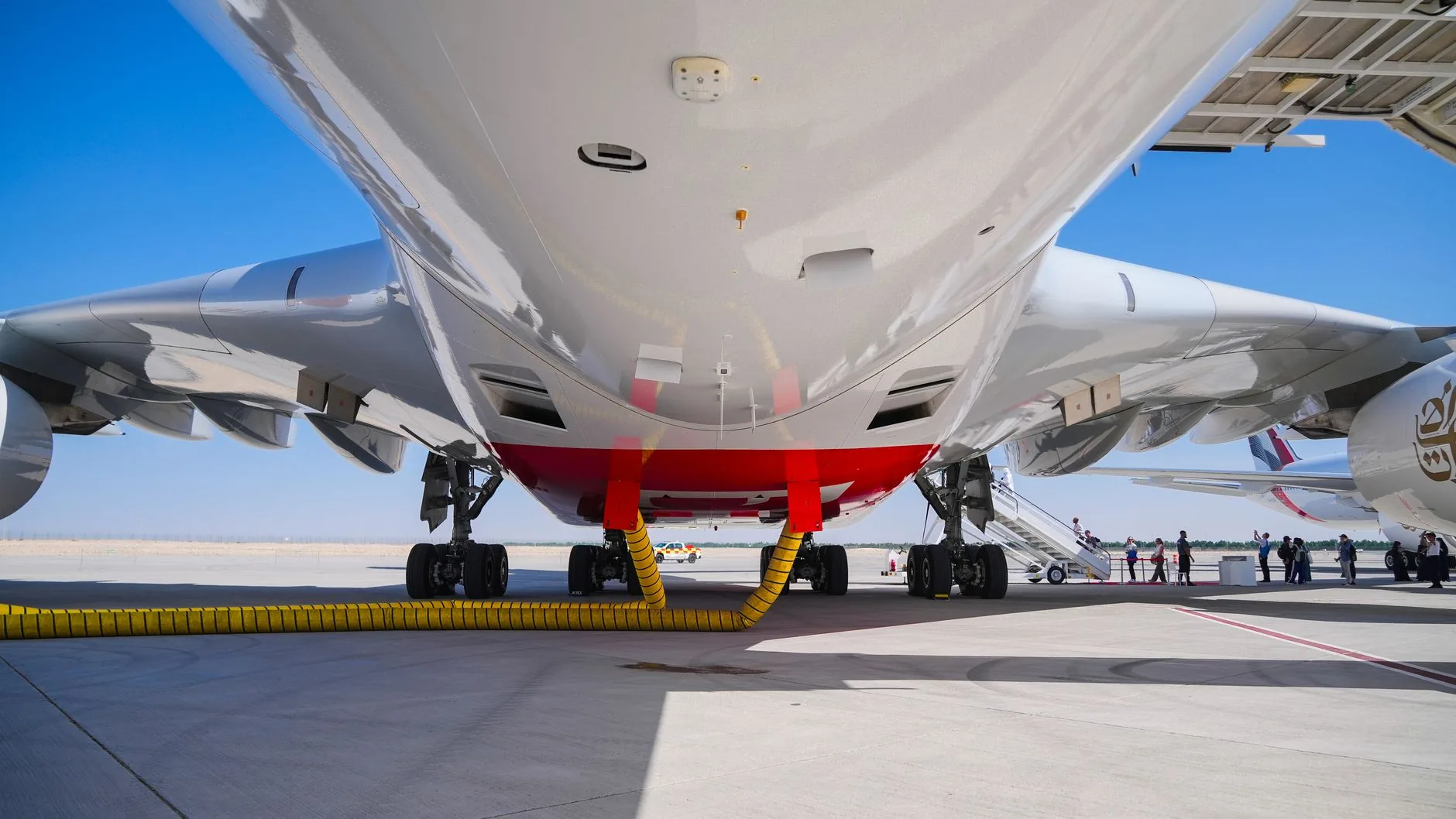 View of a large jet from below, parked at Dubai airport on a sunny day.