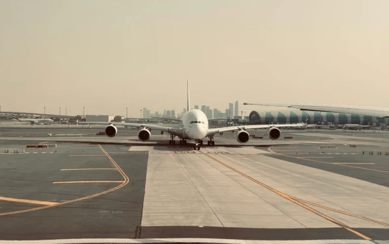 A large airplane on the tarmac at Dubai International Airport with city skyline in the background.