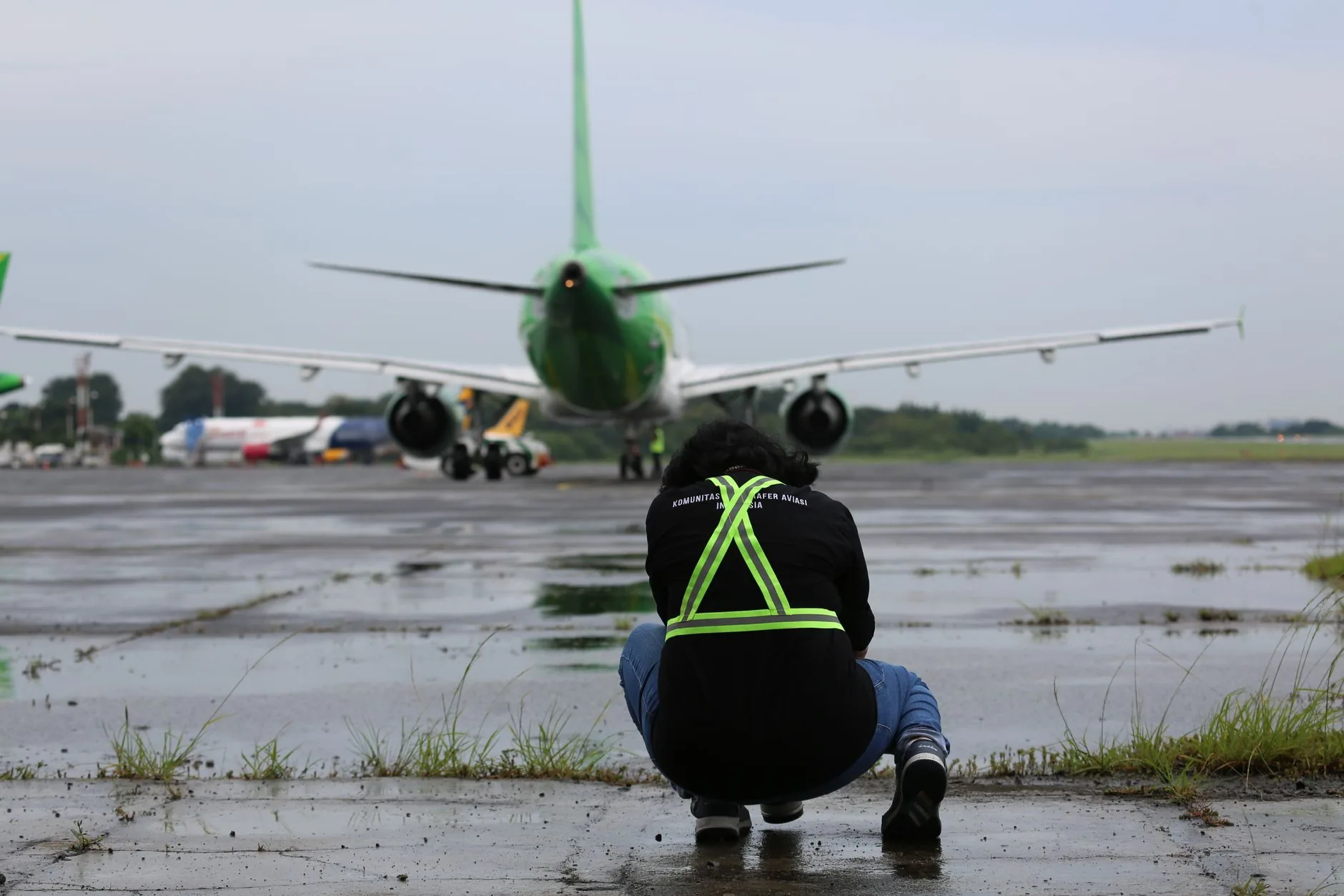 Ground crew member crouches near a taxiing airplane on a wet runway at Jakarta airport.