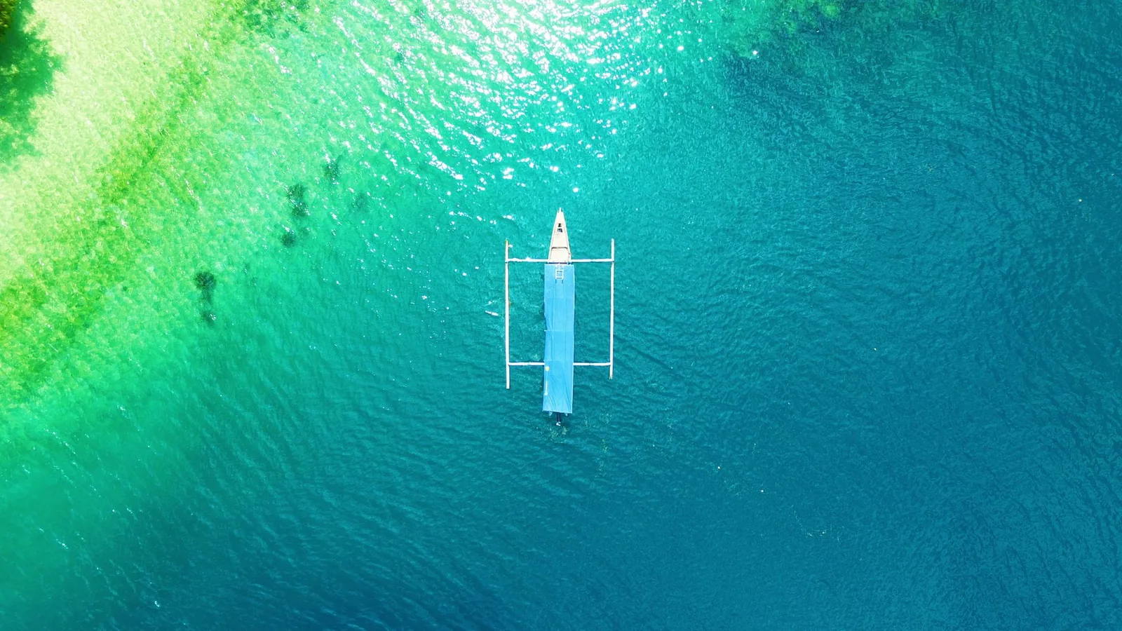 A drone capture of a boat floating on the vibrant turquoise waters of Lombok, Indonesia.