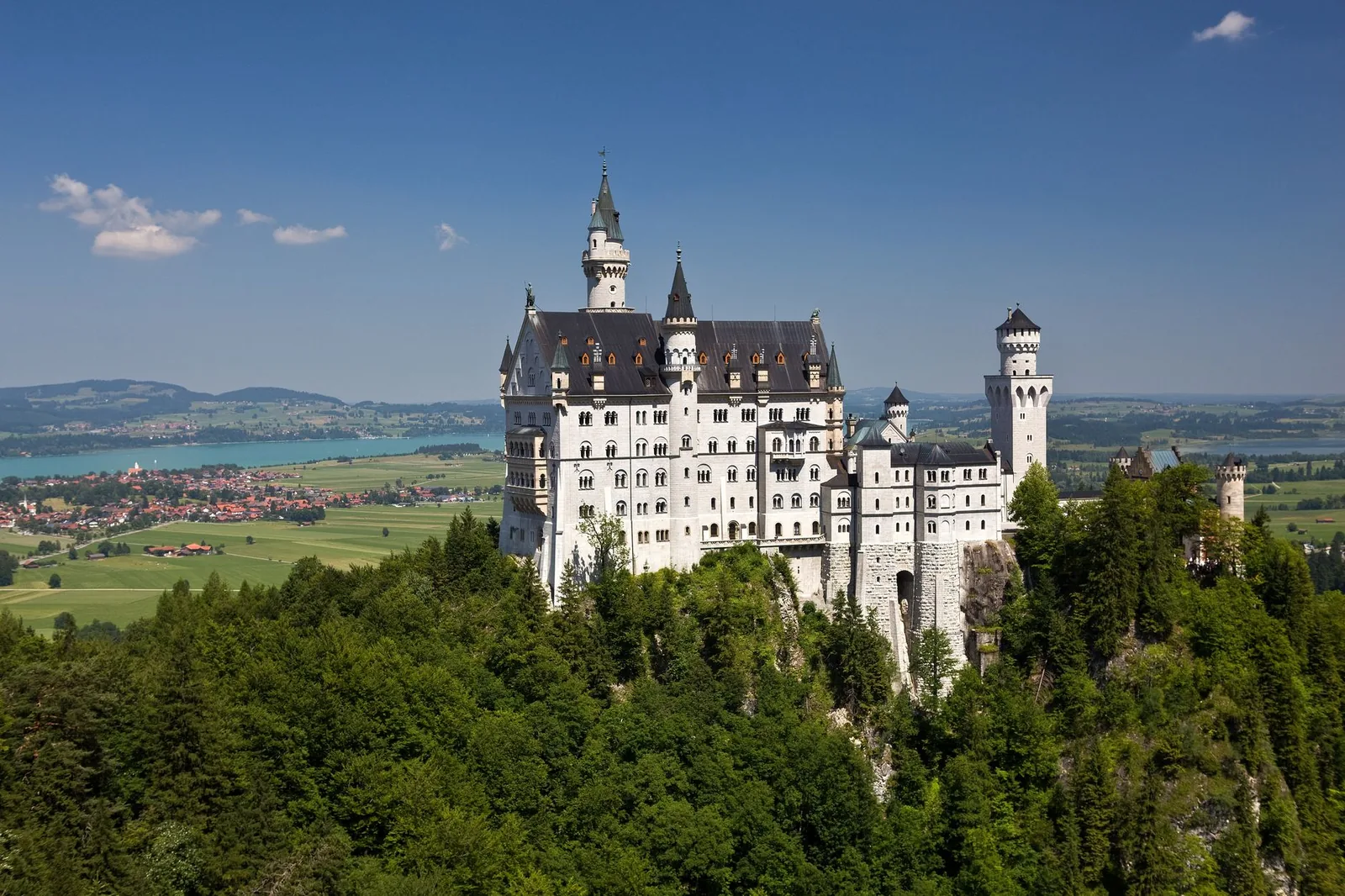 Stunning view of Neuschwanstein Castle amidst lush greenery under a clear blue sky in Bavaria, Germany.