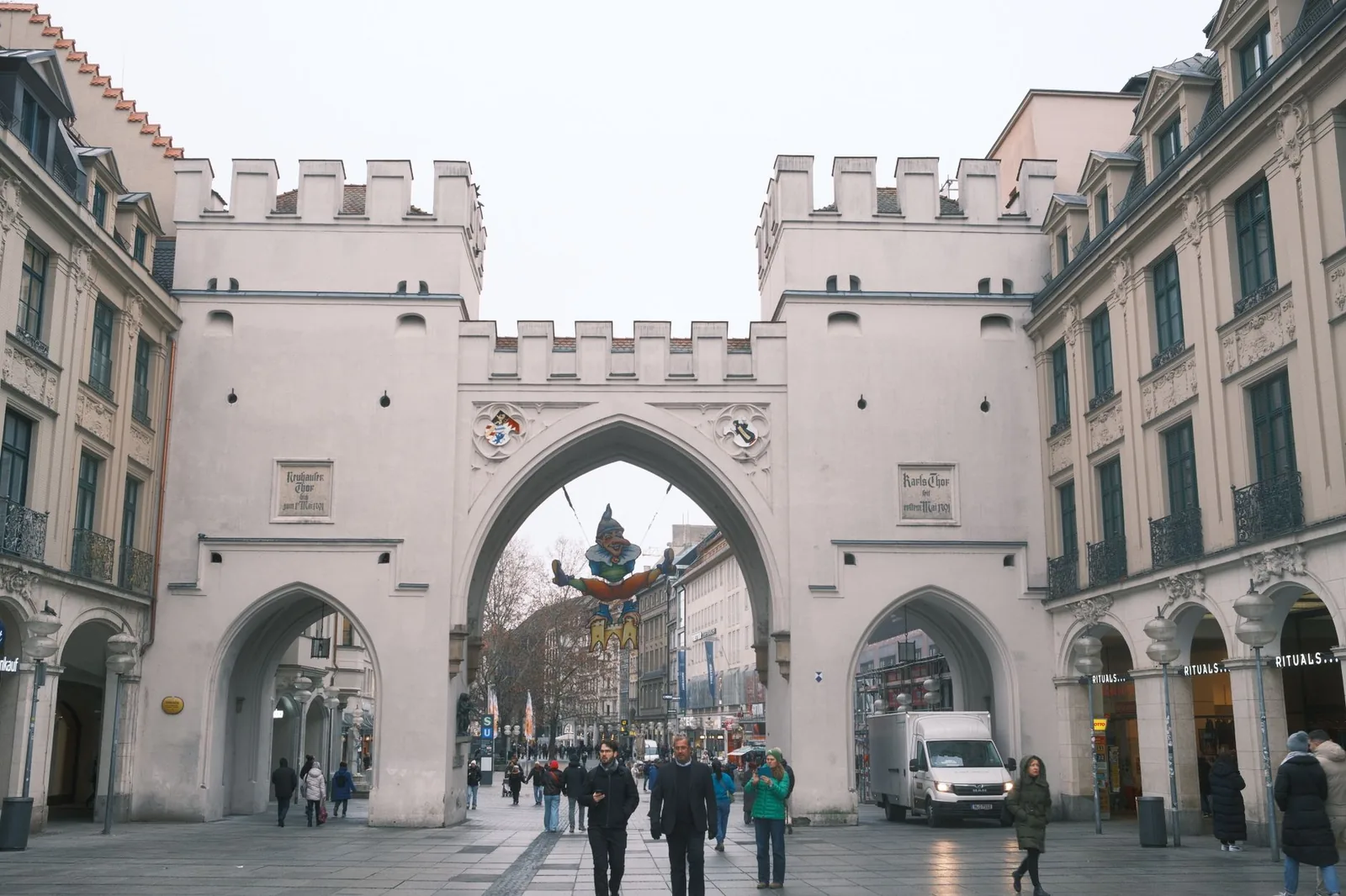View of Karlstor gate in Munich with people walking along the street on a cloudy day.