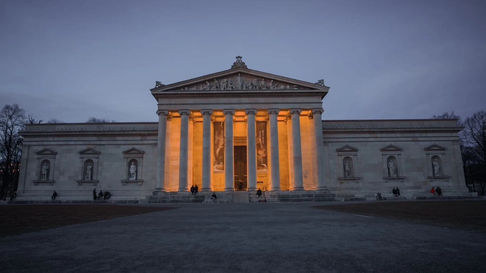 Illuminated Propylaea at dusk in Munich, Germany, showcasing neoclassical architecture.
