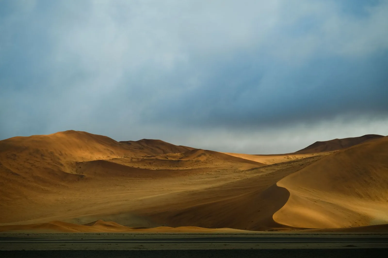 Breathtaking view of the Namib Desert sand dunes under a cloudy sky in the early morning light.