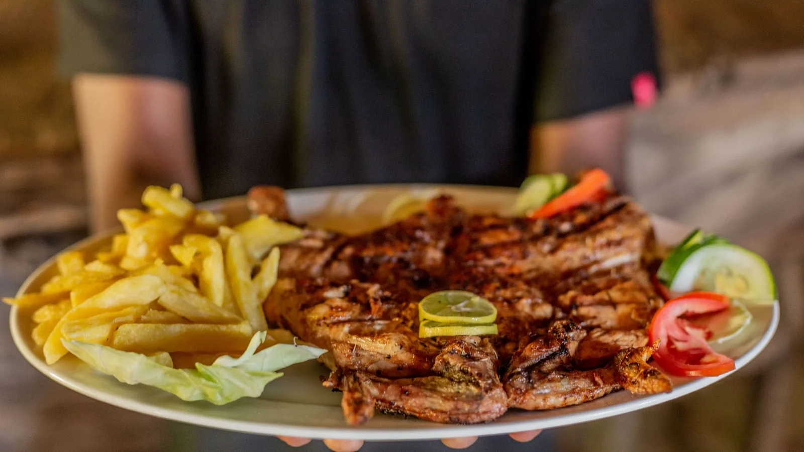 Close-up of a plate with grilled meat, fries, and fresh vegetables.