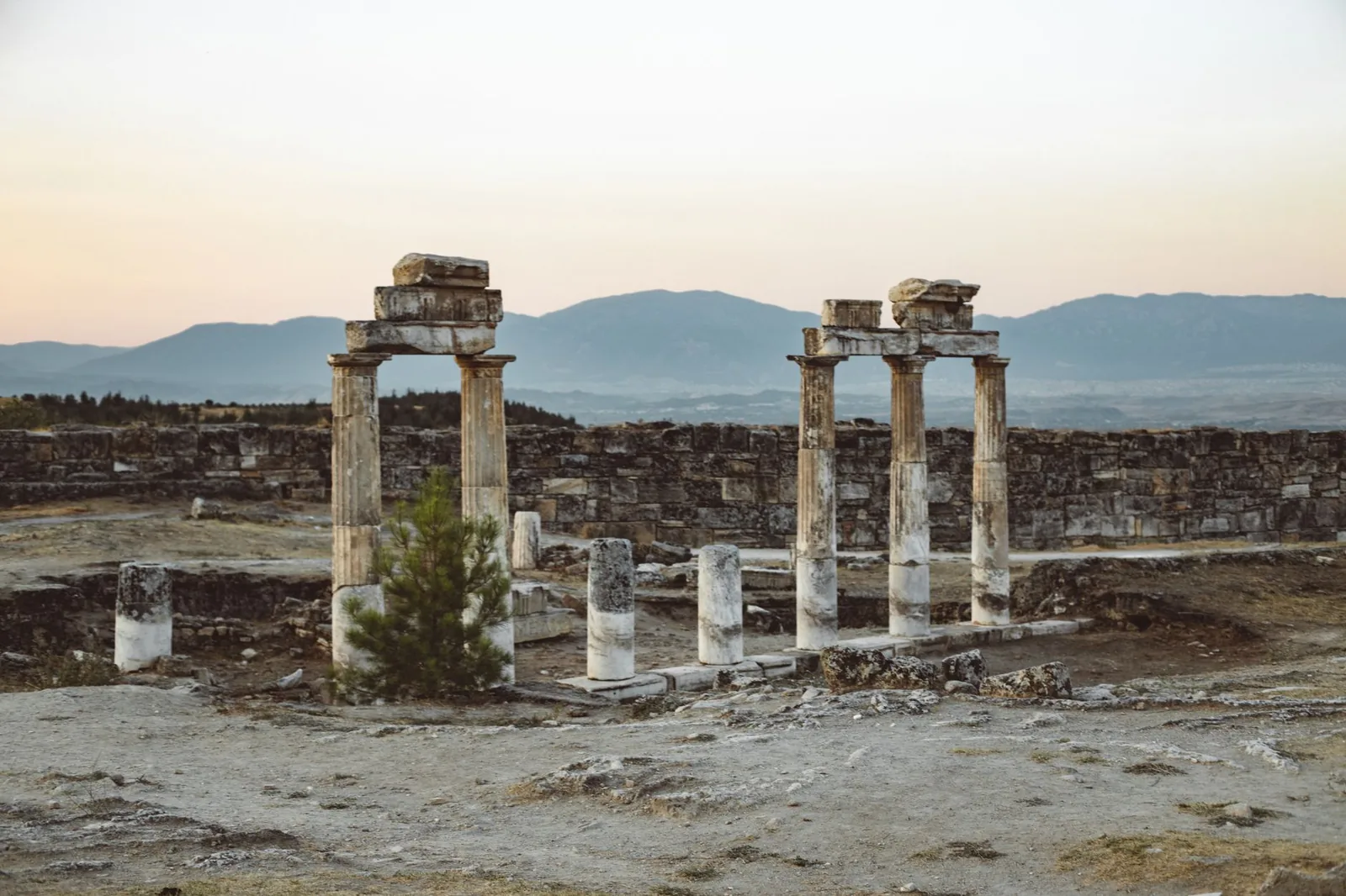 Atmospheric view of ancient Roman ruins with mountains in Pamukkale, Turkey at sunset.
