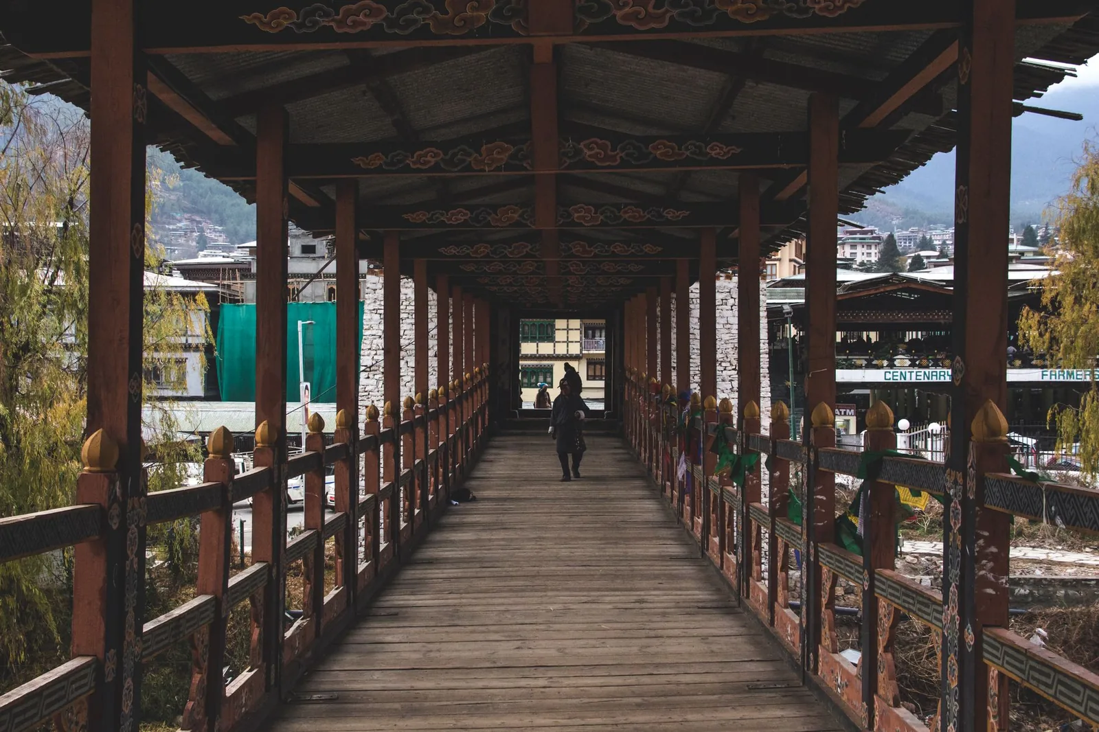 A person walks across a narrow, traditional wooden bridge in Thimphu, Bhutan, showcasing local architecture.