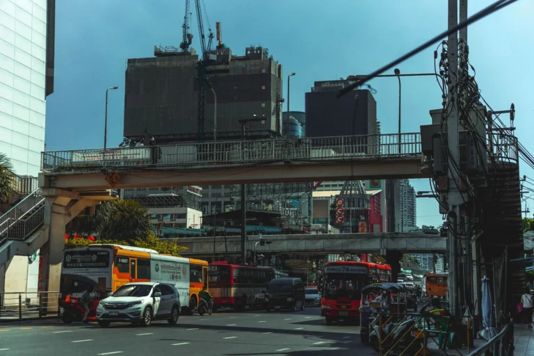 Dynamic view of Bangkok's bustling urban traffic with buses, cars, and footbridges against a city backdrop.