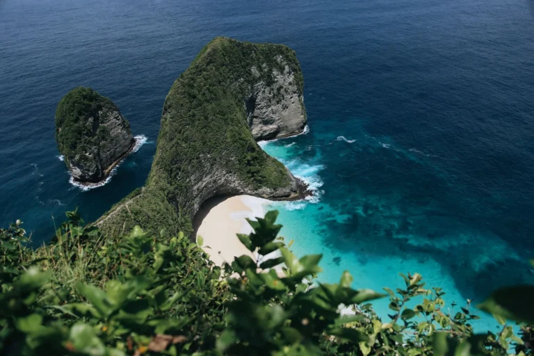 Stunning aerial view of Nusa Penida's picturesque beach in Bali surrounded by clear turquoise waters and lush green cliffs.