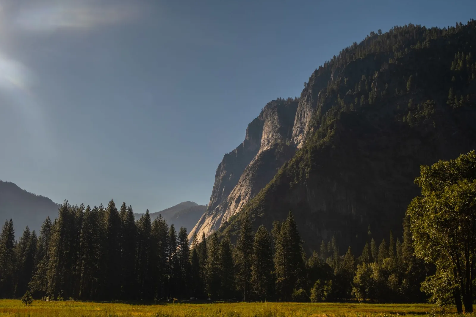 Stunning view of Yosemite Valley mountains at sunset with lush forest and clear sky.