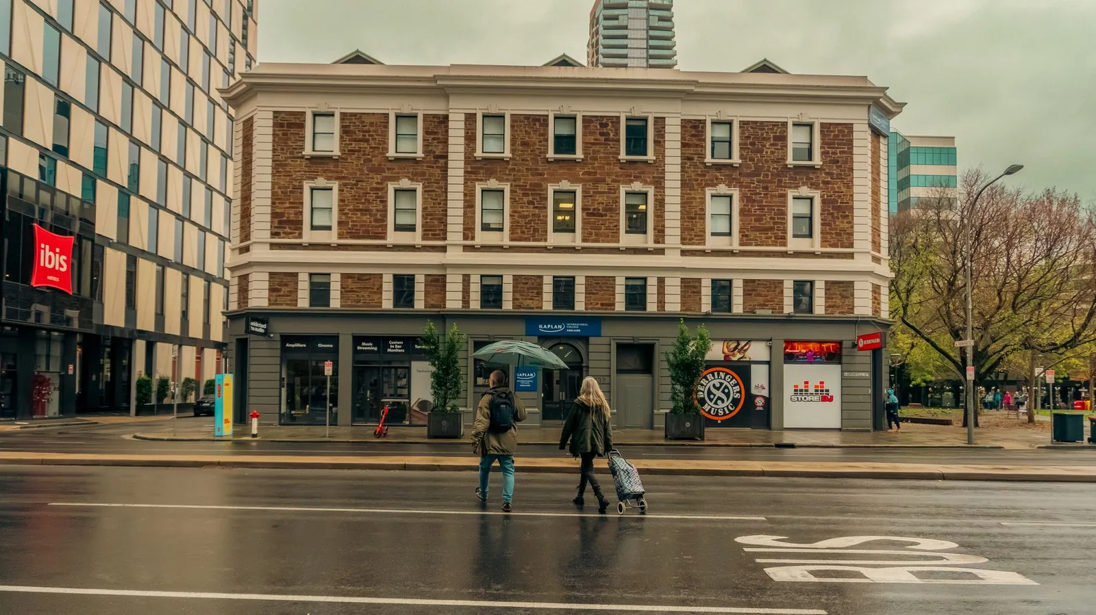 A couple walks through the wet streets of Adelaide city on a rainy day, showcasing urban life.