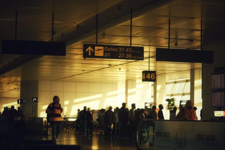 Crowded hallways and directional signs guide travelers in Delhi Airport.