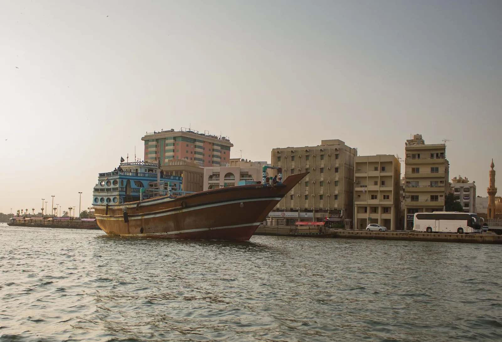 Scenic view of a traditional Arabic dhow sailing on Dubai Creek with urban skyline backdrop.