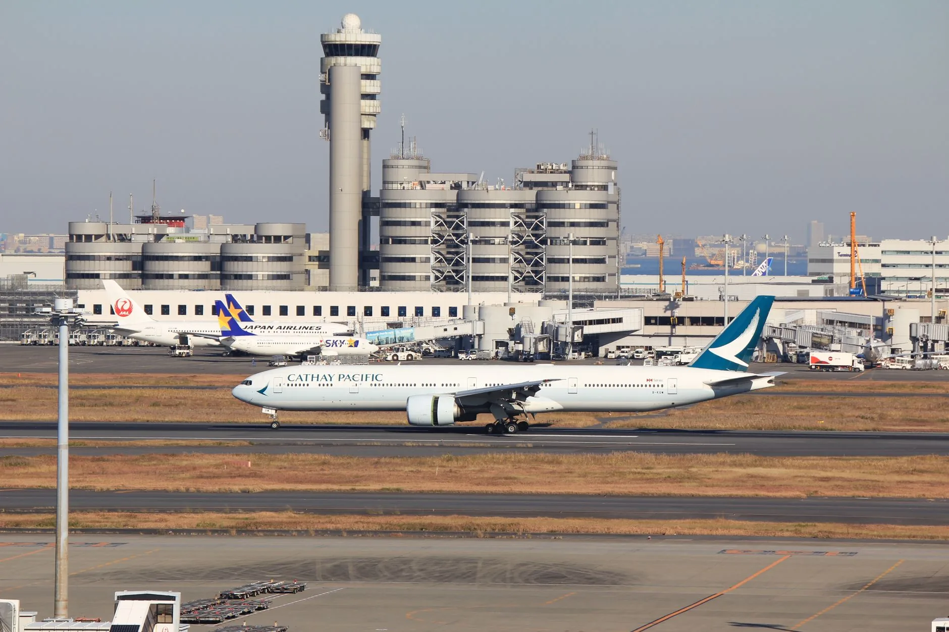 Cathay Pacific plane on runway at Narita Airport, Tokyo, with terminal and control tower in view.