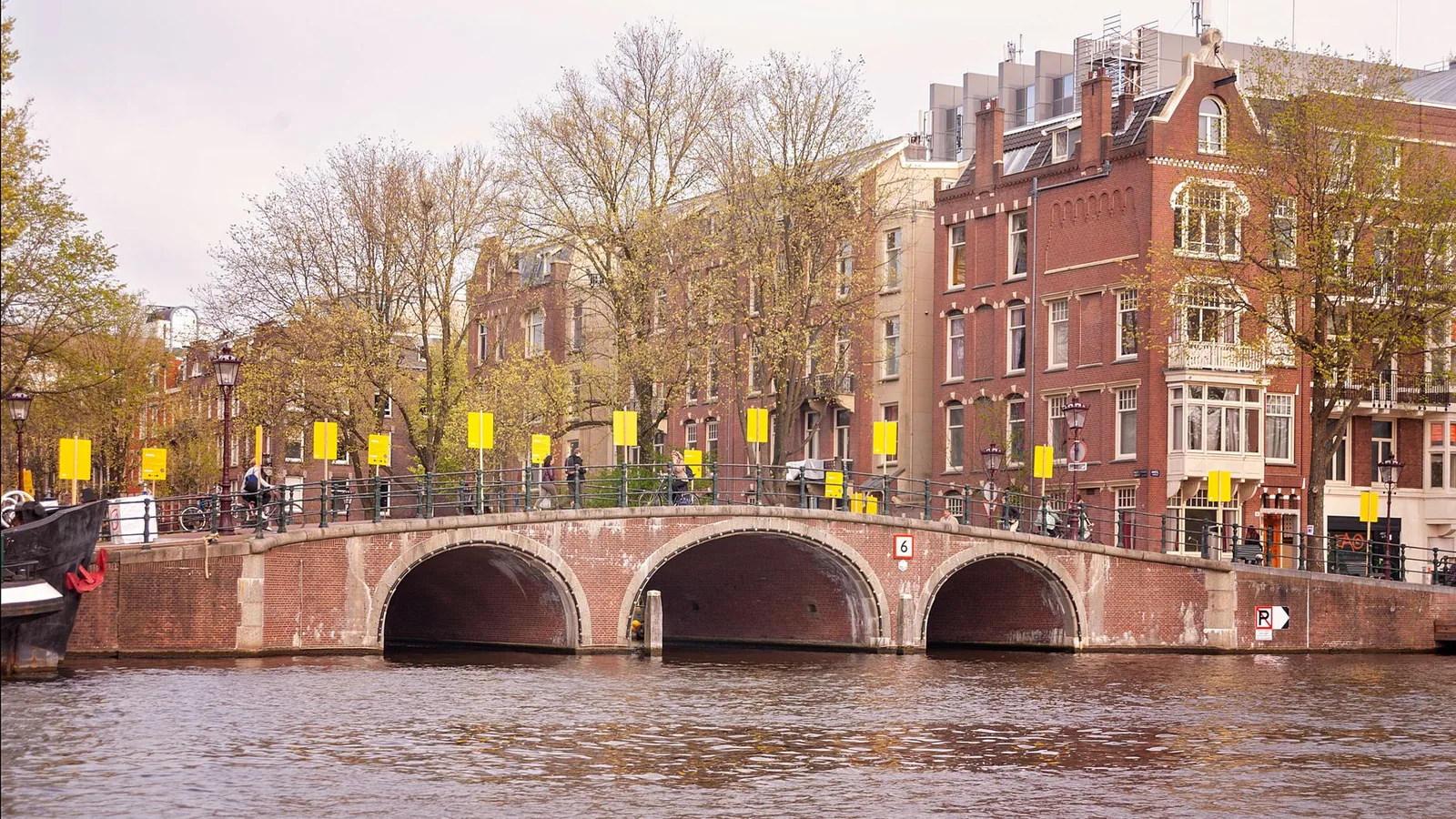 Beautiful day in Amsterdam featuring a historic brick bridge over a tranquil canal with classic architecture.