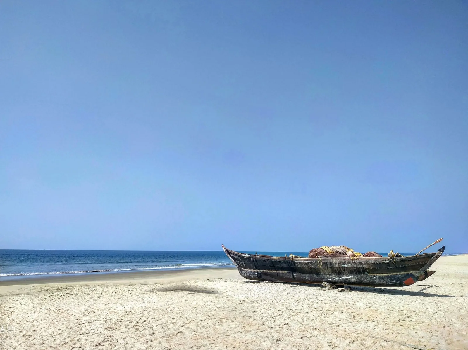 Idyllic beach scene in Goa, India with a wooden fishing boat and calm sea.