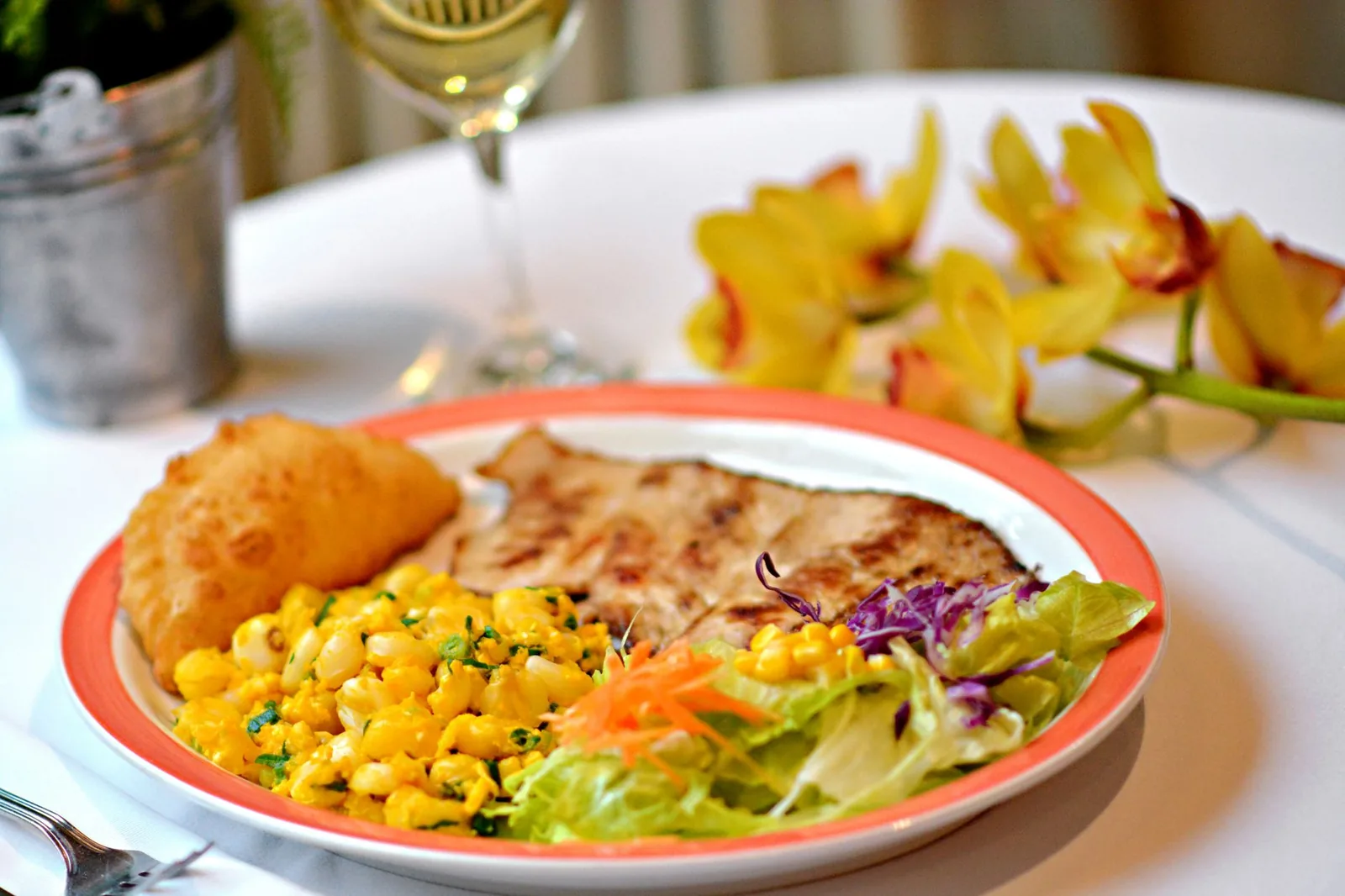 A delicious meal served with wine and complemented by vibrant flowers on a white table.