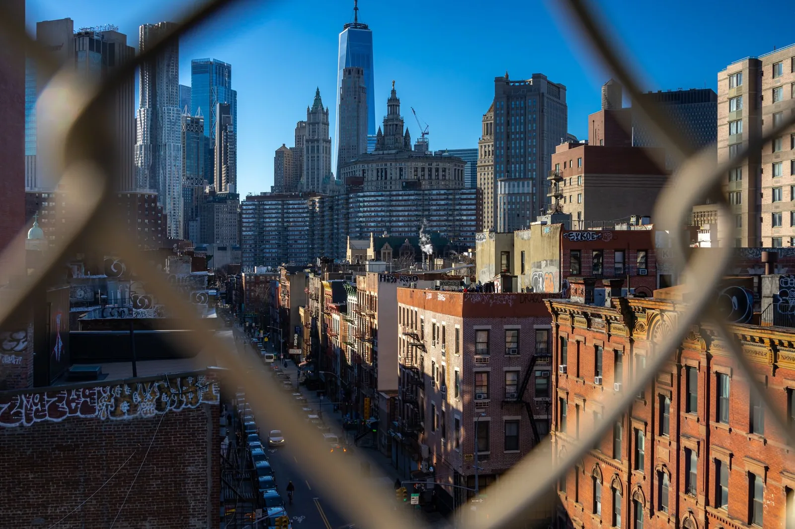 Captivating view of Lower Manhattan skyscrapers through a fence, showcasing urban architecture.