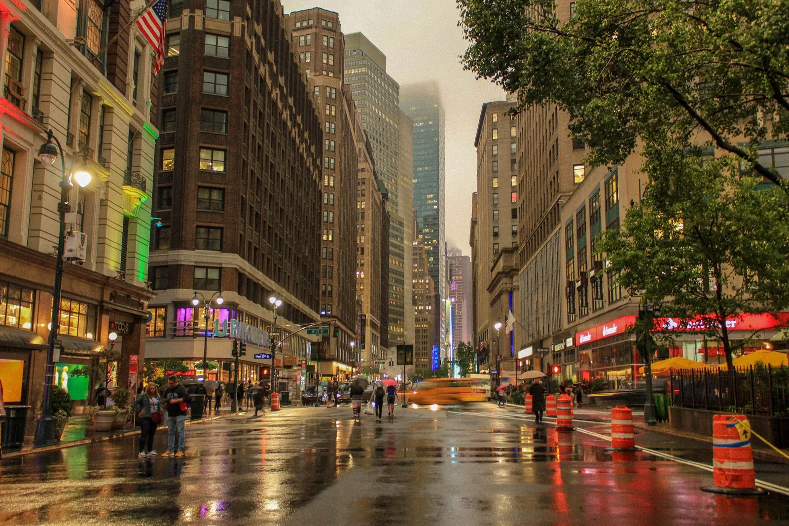 A bustling evening scene in Manhattan with illuminated buildings and reflections on wet streets.