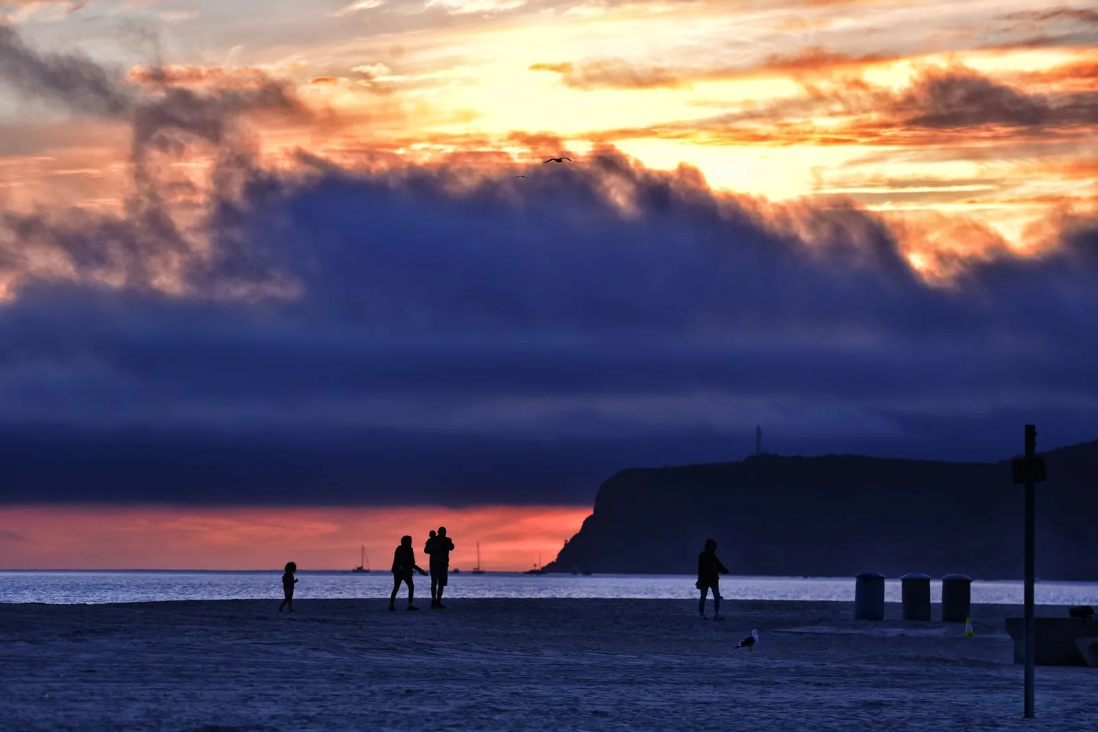 A vibrant sunset at Coronado Beach with people silhouetted against the colorful sky.