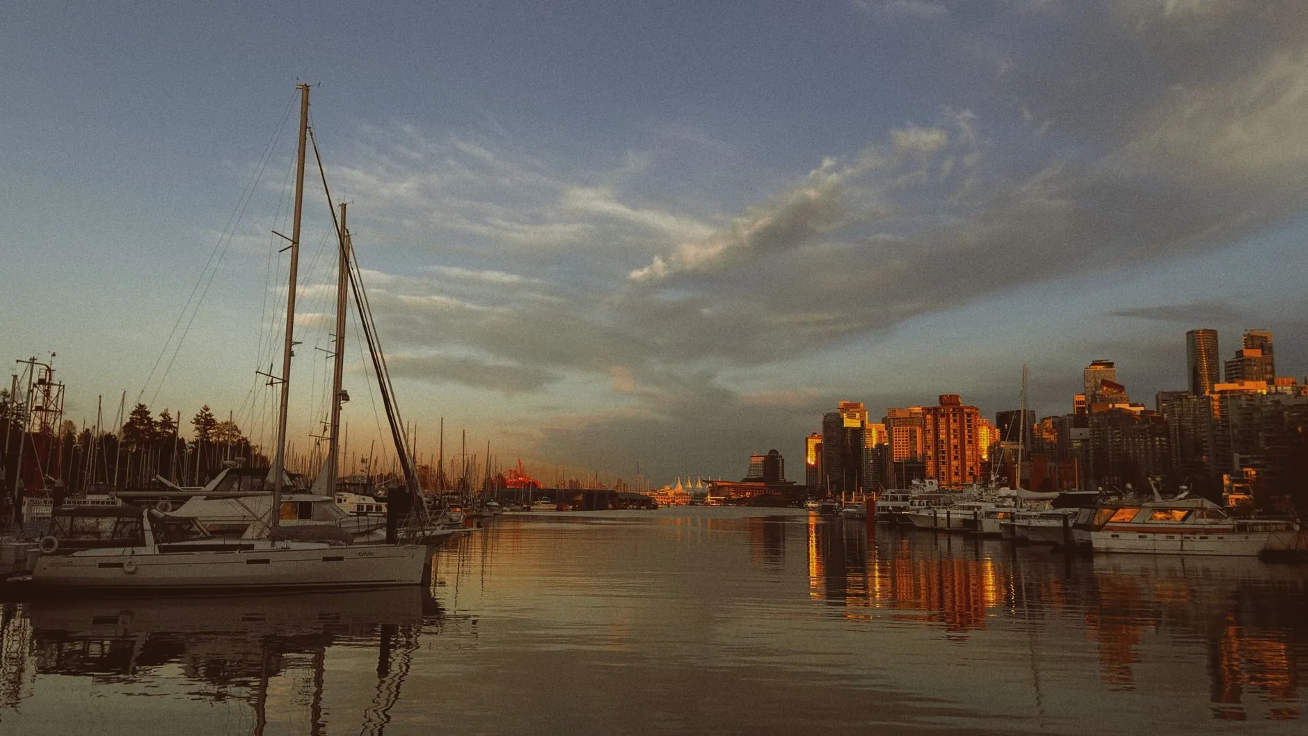 A stunning view of boats docked at a marina during golden hour, with the Vancouver skyline bathed in warm sunset light.